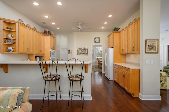 kitchen featuring dark wood-type flooring, a kitchen breakfast bar, kitchen peninsula, and white fridge