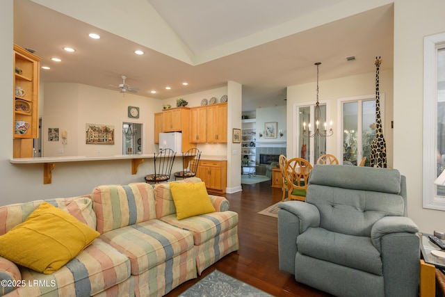 living room with a tile fireplace, lofted ceiling, dark wood-type flooring, and ceiling fan with notable chandelier