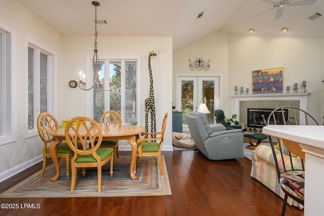 dining area featuring a tile fireplace, vaulted ceiling, ceiling fan with notable chandelier, dark hardwood / wood-style flooring, and french doors