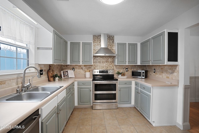 kitchen with light tile patterned flooring, wall chimney exhaust hood, sink, tasteful backsplash, and appliances with stainless steel finishes