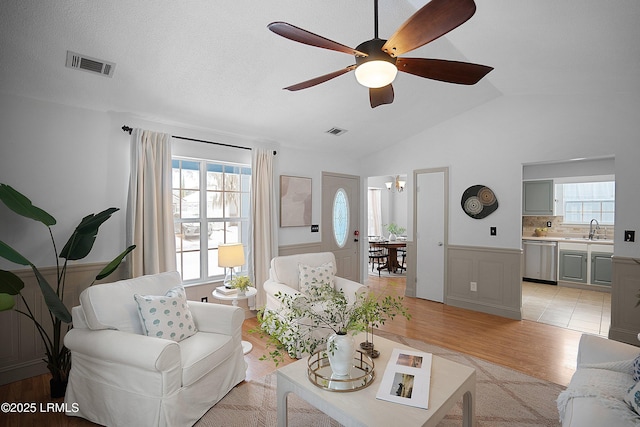 living room featuring ceiling fan with notable chandelier, lofted ceiling, light hardwood / wood-style floors, and sink