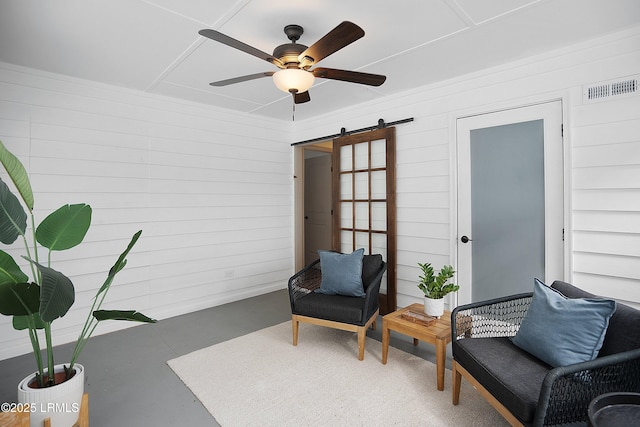 living area featuring ceiling fan, a barn door, concrete floors, and wooden walls