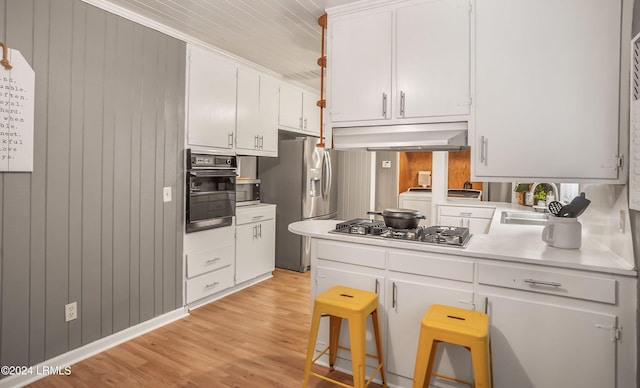 kitchen with sink, a breakfast bar, white cabinetry, wooden walls, and stainless steel appliances