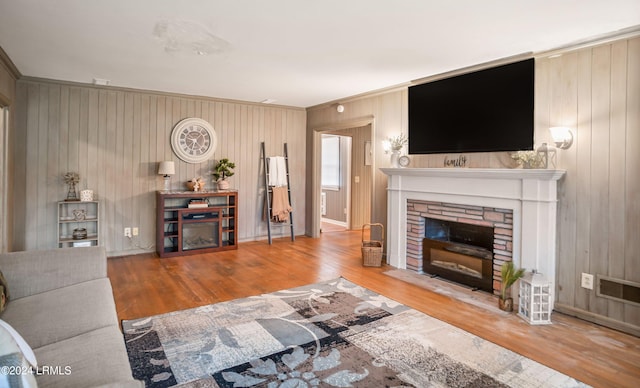 living room featuring hardwood / wood-style flooring, ornamental molding, and a stone fireplace