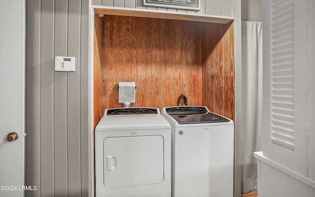 clothes washing area featuring independent washer and dryer and wood walls