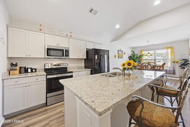 kitchen featuring visible vents, a kitchen bar, a sink, appliances with stainless steel finishes, and lofted ceiling