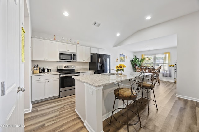 kitchen featuring visible vents, an island with sink, light wood-style flooring, appliances with stainless steel finishes, and a sink