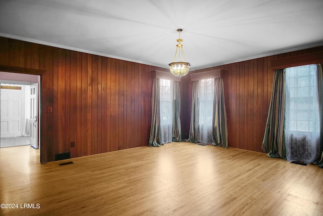 empty room with a notable chandelier, ornamental molding, and wood walls