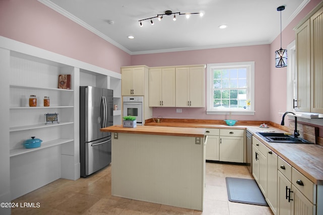 kitchen featuring wood counters, sink, hanging light fixtures, stainless steel appliances, and cream cabinetry