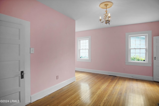 unfurnished room featuring a healthy amount of sunlight, a notable chandelier, and light hardwood / wood-style floors