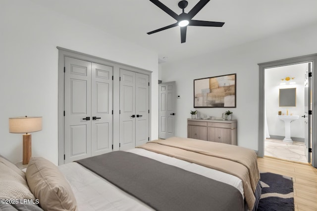 bedroom with ensuite bathroom, a sink, a ceiling fan, multiple closets, and light wood-type flooring