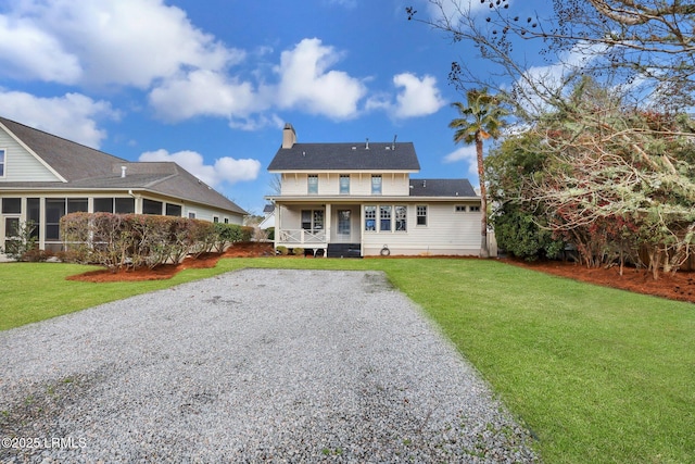 back of house featuring a porch, a sunroom, a lawn, a chimney, and gravel driveway