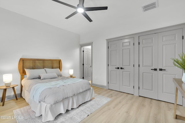 bedroom featuring baseboards, visible vents, ceiling fan, light wood-type flooring, and multiple closets