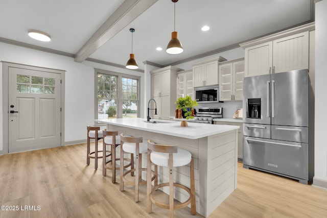 kitchen featuring a sink, light countertops, appliances with stainless steel finishes, an island with sink, and glass insert cabinets