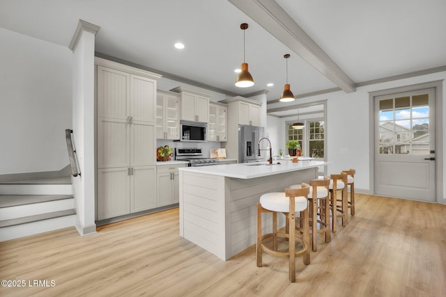 kitchen featuring a center island with sink, a kitchen breakfast bar, stainless steel appliances, light countertops, and pendant lighting