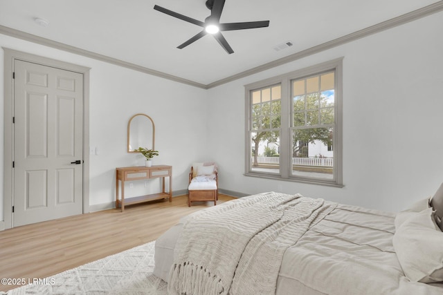 bedroom with baseboards, light wood-type flooring, visible vents, and crown molding