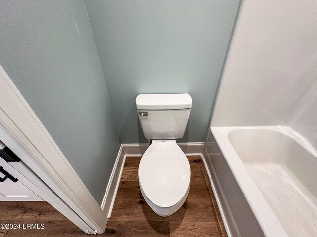 bathroom with wood-type flooring, a tub, and toilet