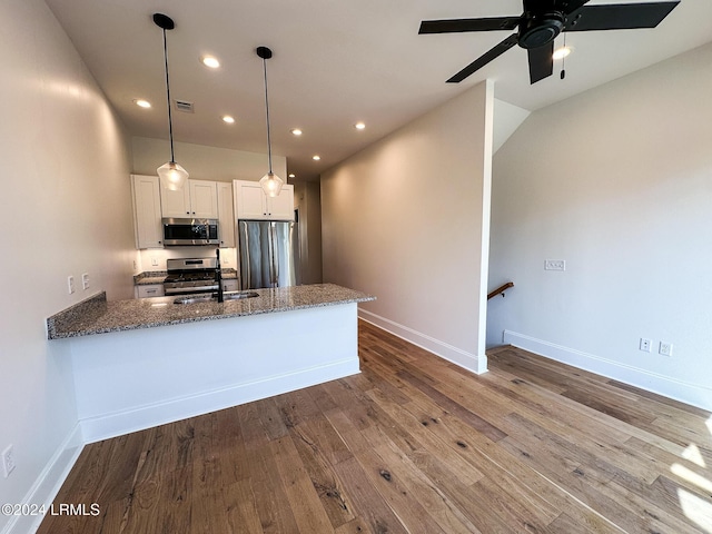 kitchen featuring hardwood / wood-style flooring, appliances with stainless steel finishes, white cabinetry, kitchen peninsula, and dark stone counters