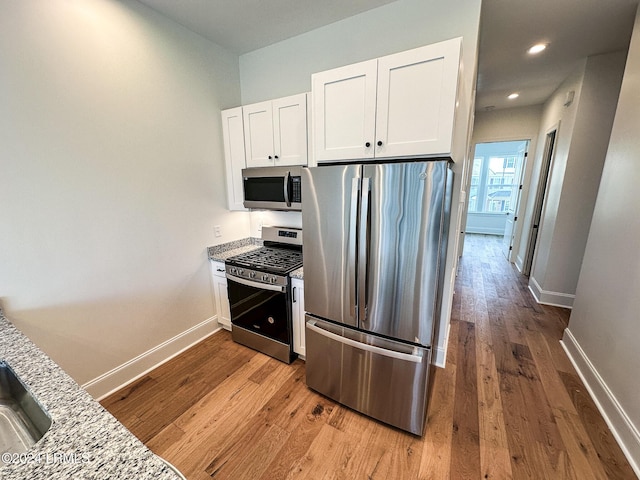 kitchen featuring appliances with stainless steel finishes, white cabinets, light stone counters, and light hardwood / wood-style floors