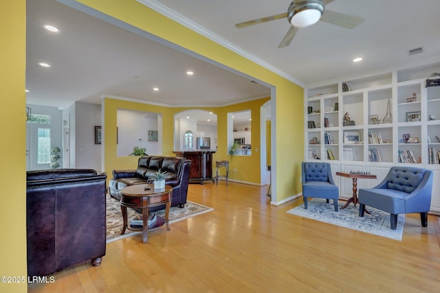 living room with built in features, light hardwood / wood-style flooring, ornamental molding, and ceiling fan