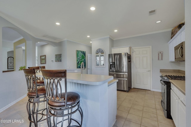 kitchen with appliances with stainless steel finishes, ornamental molding, an island with sink, white cabinets, and light tile patterned flooring