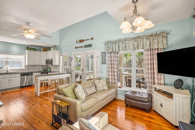 living area featuring light wood-style flooring, ceiling fan with notable chandelier, baseboards, and vaulted ceiling
