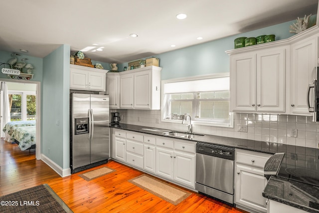 kitchen with appliances with stainless steel finishes, white cabinetry, a sink, light wood-style floors, and backsplash
