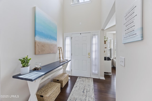 entrance foyer featuring baseboards, a wealth of natural light, dark wood-type flooring, and a towering ceiling