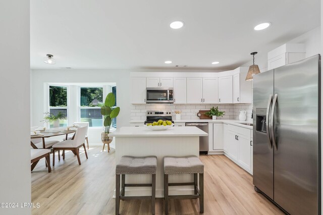 kitchen featuring a breakfast bar, hanging light fixtures, stainless steel appliances, white cabinets, and decorative backsplash