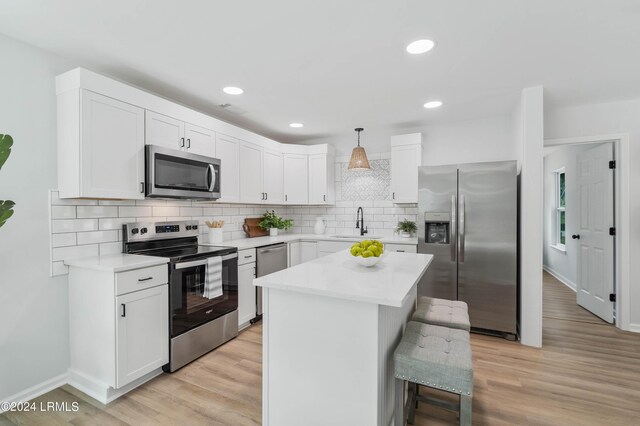 kitchen with a kitchen island, pendant lighting, sink, stainless steel appliances, and light wood-type flooring