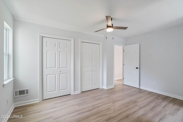 unfurnished bedroom featuring multiple closets, light wood-type flooring, ceiling fan, and multiple windows