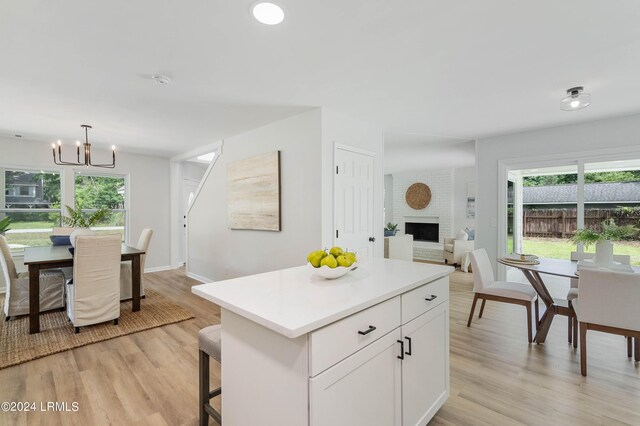 kitchen featuring pendant lighting, a fireplace, white cabinets, a kitchen island, and light wood-type flooring