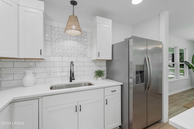 kitchen with pendant lighting, sink, stainless steel fridge, white cabinetry, and decorative backsplash