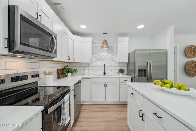 kitchen featuring pendant lighting, sink, white cabinetry, stainless steel appliances, and decorative backsplash