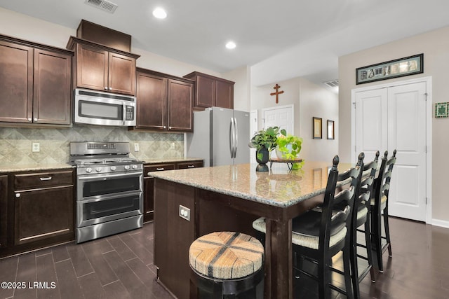 kitchen with appliances with stainless steel finishes, a breakfast bar area, backsplash, and light stone counters