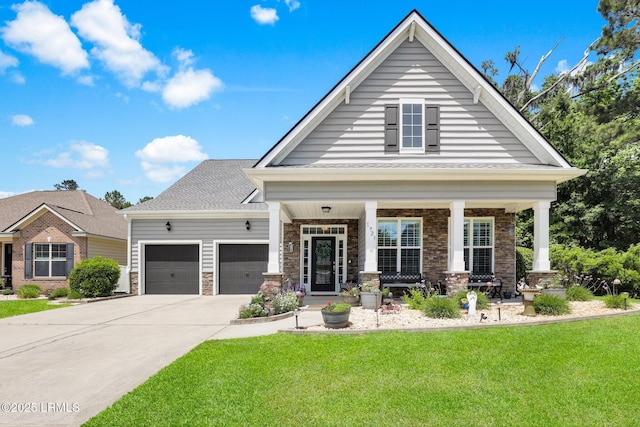 view of front of house featuring a front lawn, stone siding, an attached garage, driveway, and a porch