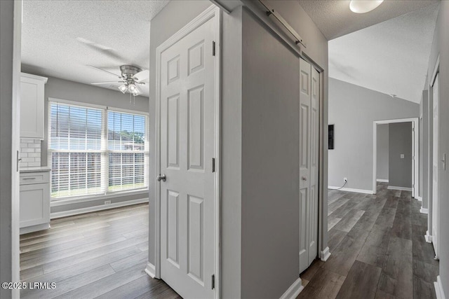 corridor featuring a textured ceiling, dark wood-style flooring, and baseboards