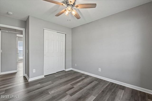 unfurnished bedroom featuring dark wood-type flooring, a closet, baseboards, and a ceiling fan