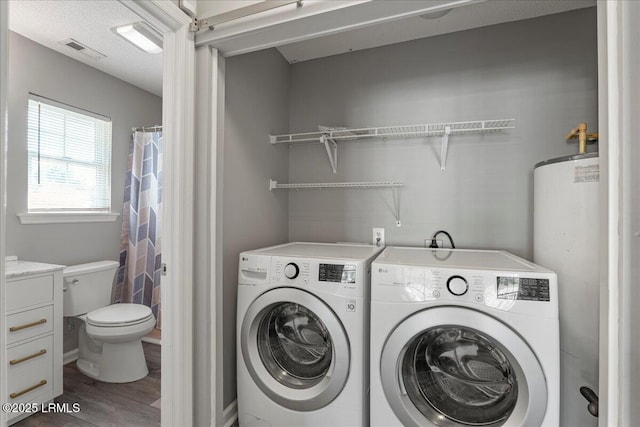 clothes washing area featuring washing machine and clothes dryer, wood finished floors, and water heater