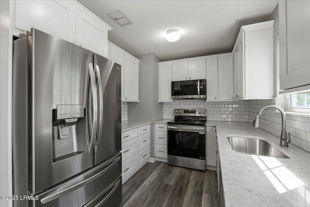 kitchen with appliances with stainless steel finishes, a sink, white cabinets, decorative backsplash, and a textured ceiling