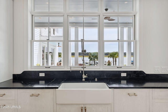 70 Brams Point Rd, Hilton Head Island, SC 29926 - kitchen with dark countertops, a sink, white cabinetry, and a water view