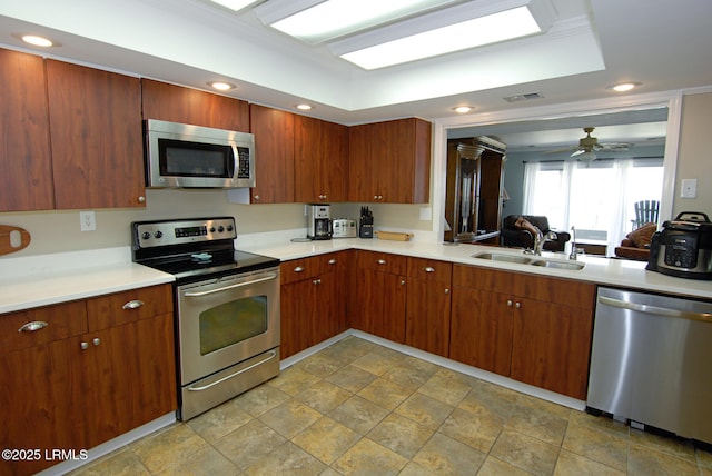 kitchen with a ceiling fan, stone finish flooring, appliances with stainless steel finishes, a sink, and light countertops