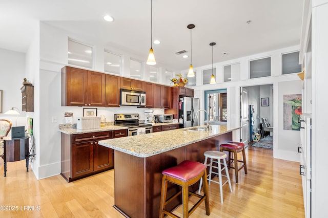 kitchen featuring a breakfast bar area, hanging light fixtures, stainless steel appliances, light wood-type flooring, and a sink