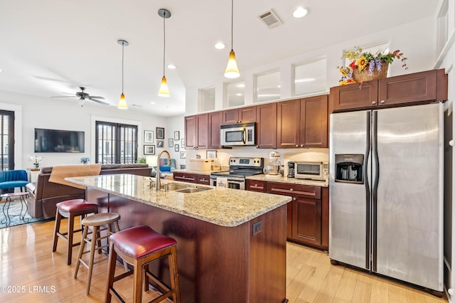 kitchen featuring stainless steel appliances, visible vents, open floor plan, a sink, and light wood-type flooring