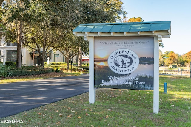 community / neighborhood sign featuring aphalt driveway and a lawn