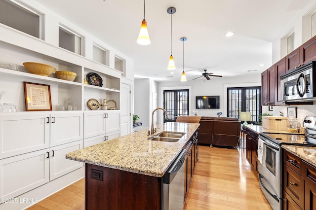 kitchen with stainless steel appliances, a sink, light wood-style floors, an island with sink, and pendant lighting