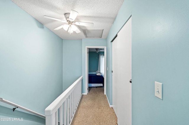 hall with a textured ceiling, an upstairs landing, light carpet, and attic access