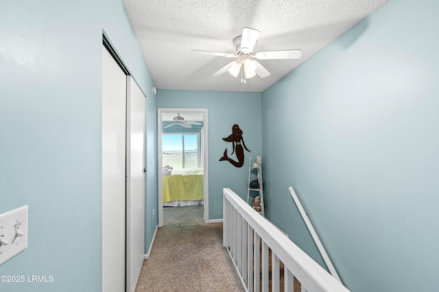 hall with carpet floors, a textured ceiling, and an upstairs landing