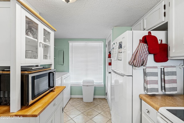 kitchen with a textured ceiling, light tile patterned floors, butcher block counters, glass insert cabinets, and white appliances