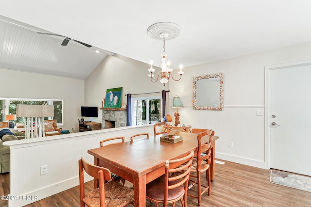 dining space with lofted ceiling, a fireplace, a chandelier, and light hardwood / wood-style floors